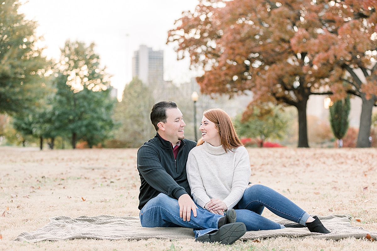 Couple cuddling and kissing on blanket at Tulsa Centennial Park engagement